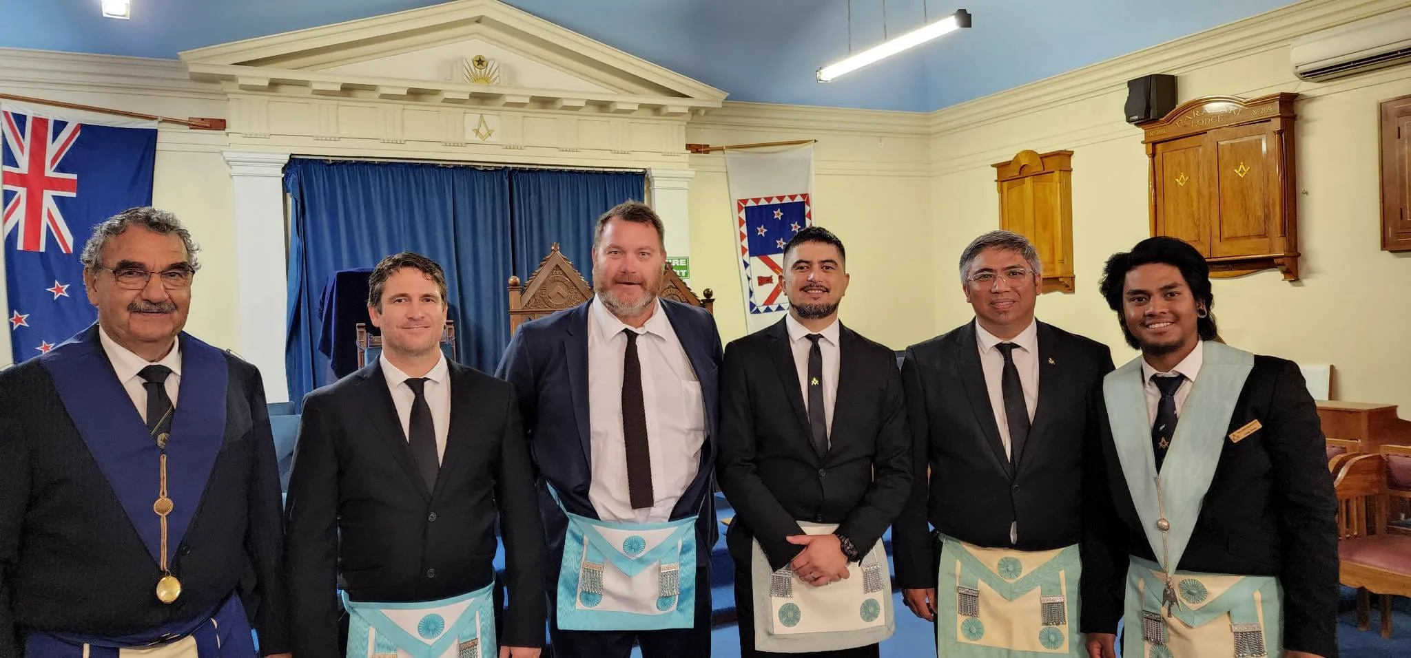 Six Freemasons in regalia standing together in the lodge room
